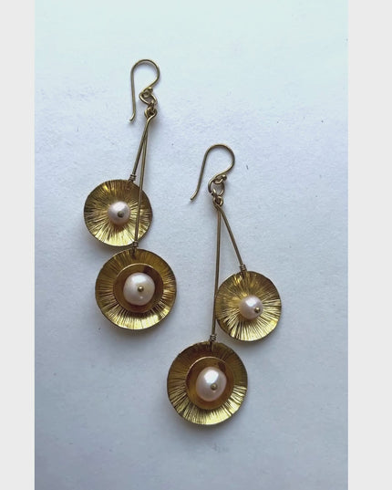 These dangling earrings have a unique design with a double drop with a round organic shape suspended at the bottom containing a pearl in the middle.